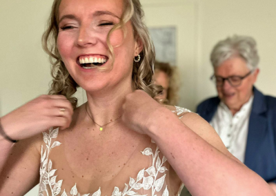 Lachende bruid tijdens het omdoen van haar sieraden